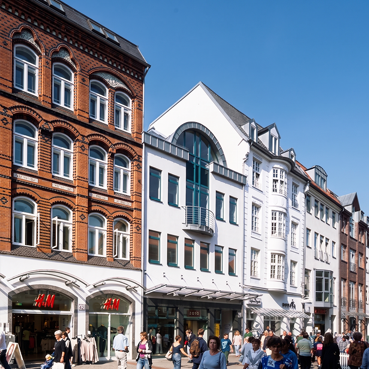 Zu sehen ist eine Einkaufsstraße in der Stadt Flensburg (SH) mit einer Mixed-use Immobilie mit einem H&M-Store sowie darüberliegenden Wohnungen; ein Referenzobjekt der Firma unimo real estate concepts