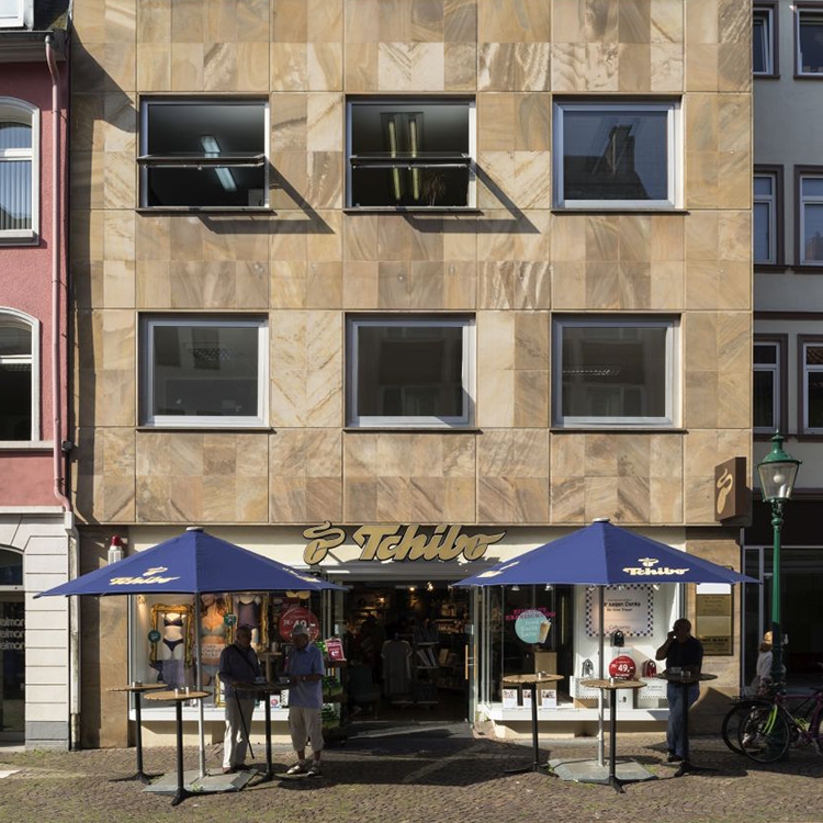 Zu sehen ist eine Mixed-use Immobilie in der Stadt Fulda (Hessen) mit einer Tchibo-Filiale sowie darüberliegenden Wohnungen; ein Referenzobjekt der Firma unimo real estate concepts
