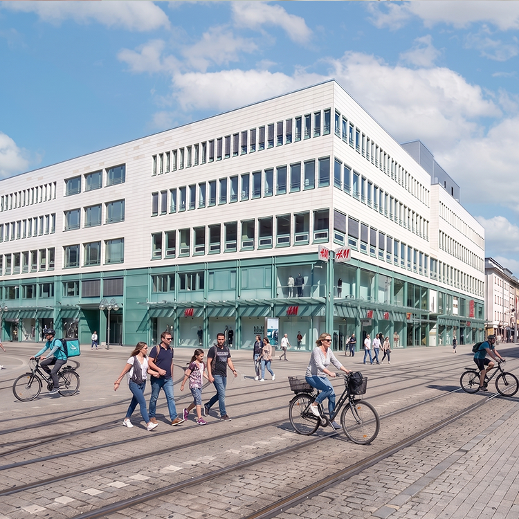 Zu sehen ist eine Gewerbeimmobilie in Mannheim (BaWü), gelegen in der Haupteinkaufsstraße „Planken“ mit einer H&M-Filiale sowie Büros; ein Referenzobjekt der Firma unimo real estate concepts
