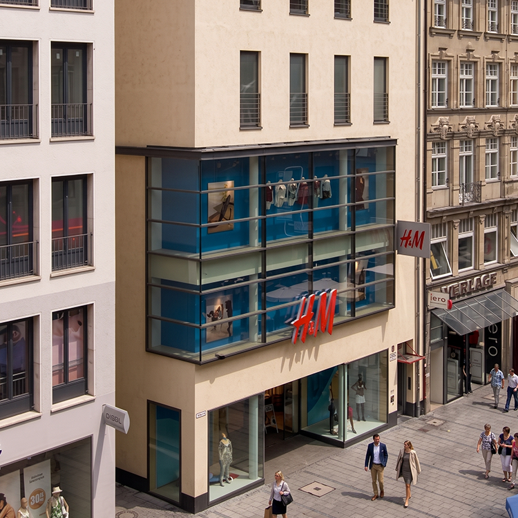 Zu sehen ist eine Mixed-use Immobilie in München (Bayern) mit einer H&M-Filiale sowie darüberliegenden Wohnungen; ein Referenzobjekt der Firma unimo real estate concepts