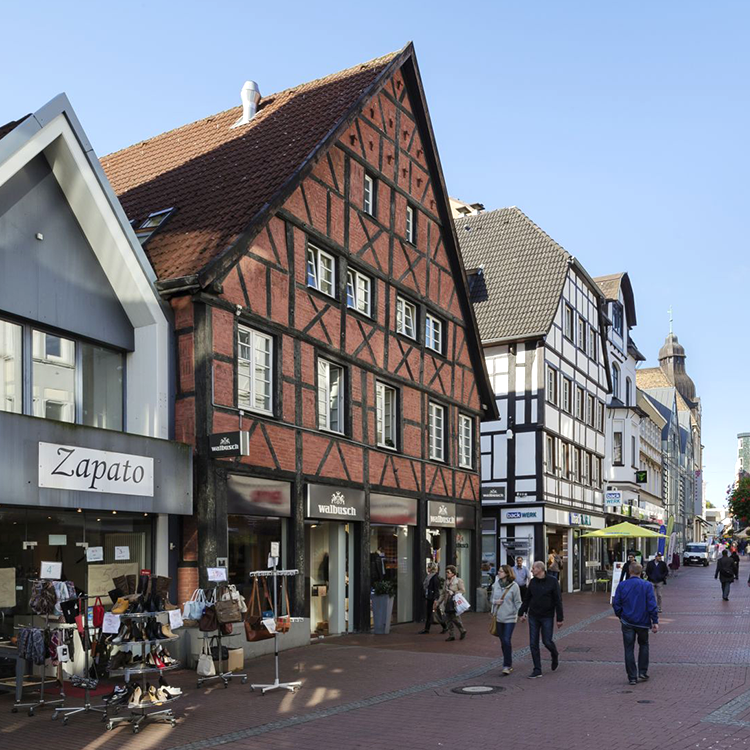 Zu sehen ist eine Einkaufsstraße in der Stadt Recklinghausen (NRW) mit einer Mixed-use Immobilie mit einem Walbusch-Store sowie darüberliegenden Wohnungen; ein Referenzobjekt der Firma unimo real estate concepts
